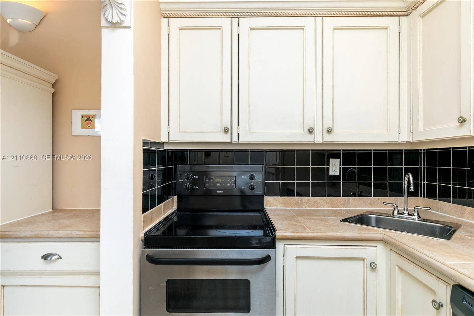 3121 S Ocean Drive, #209, Hallandale Beach, FL 33009 Kitchen featuring white cabinetry with crown molding, black tile backsplash, stainless steel range, and stone-finish countertops with an integrated stainless steel sink