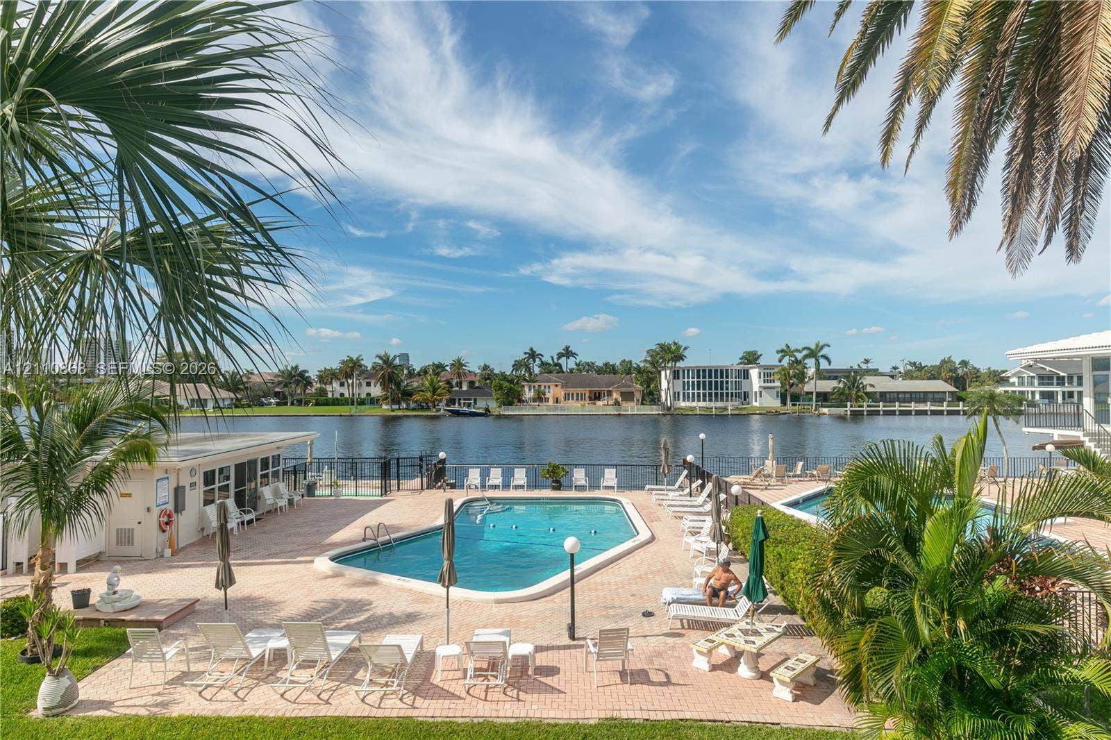 3121 S Ocean Drive, #209, Hallandale Beach, FL 33009 Waterfront pool area featuring a paver deck, metal perimeter fencing, and mature palm trees