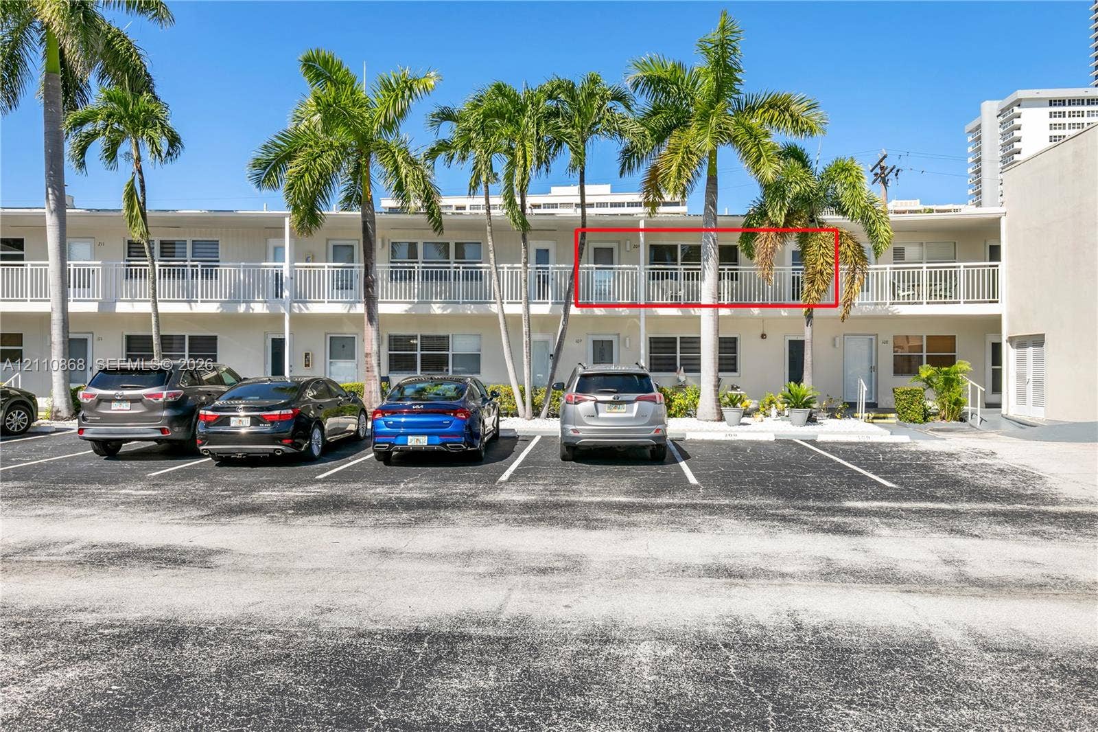 3121 S Ocean Drive, #209, Hallandale Beach, FL 33009 Two-story residential building featuring a second-level exterior balcony with white metal railings, integrated surface parking, and mature palm trees