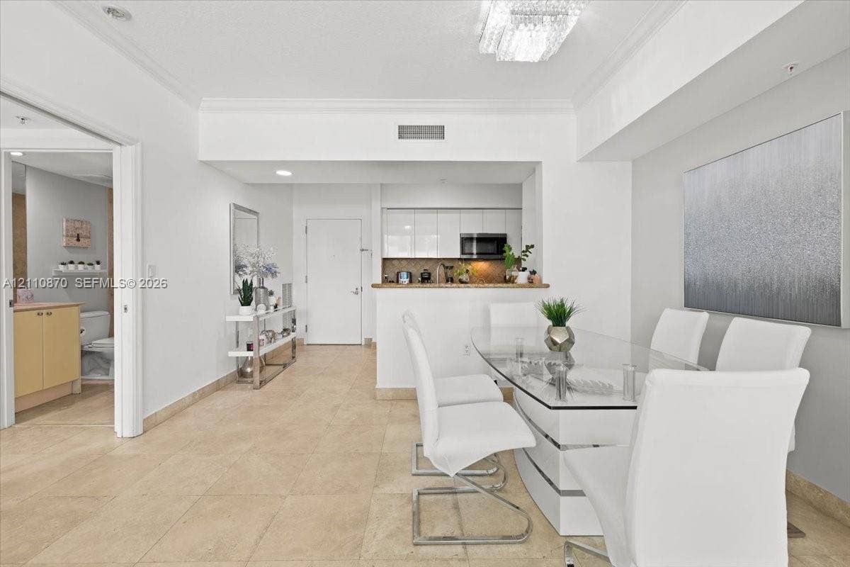1755 E Hallandale Beach Boulevard, #MEZ5E, Hallandale Beach, FL 33009 Open-concept floor plan featuring neutral stone-finish tile flooring, a tiered tray ceiling with a crystal-style chandelier, and high-gloss white cabinetry