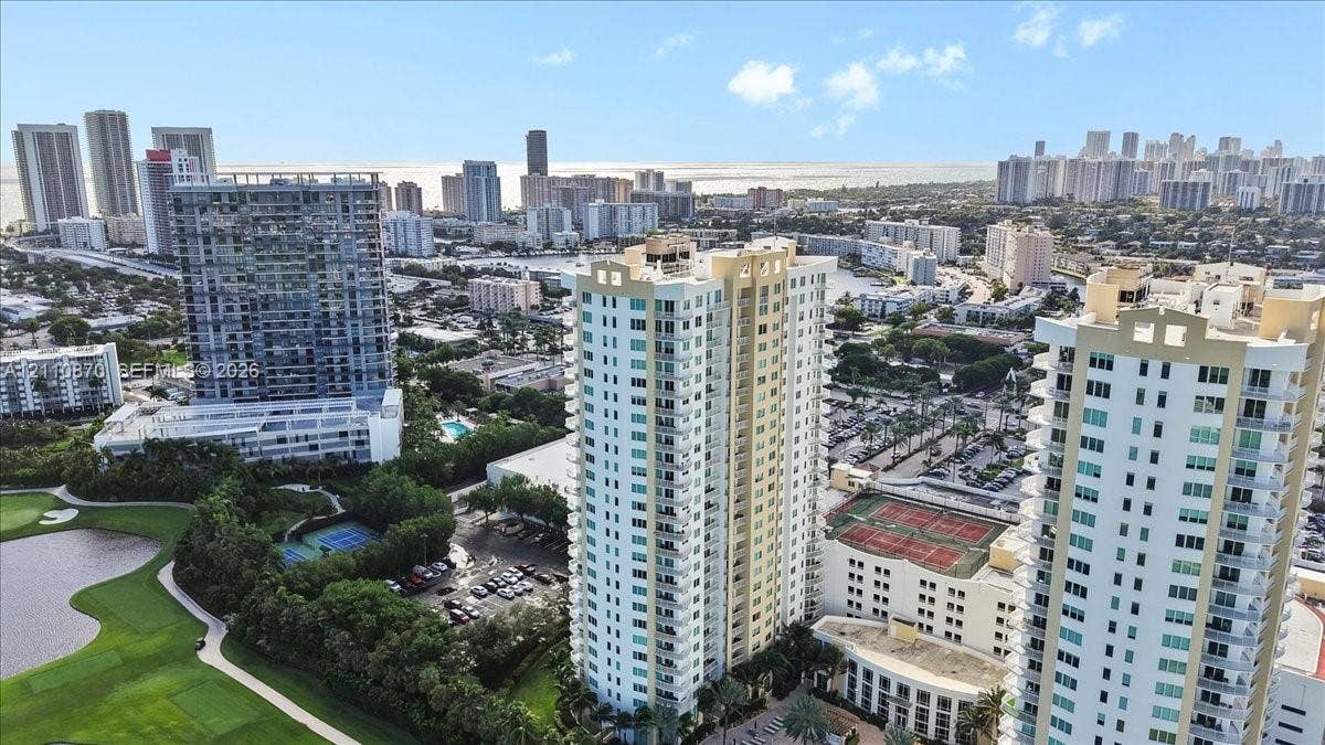 1755 E Hallandale Beach Boulevard, #MEZ5E, Hallandale Beach, FL 33009 High-rise residential tower featuring wraparound balconies, multi-story glass-paned windows, tennis courts, and proximity to an expansive golf course