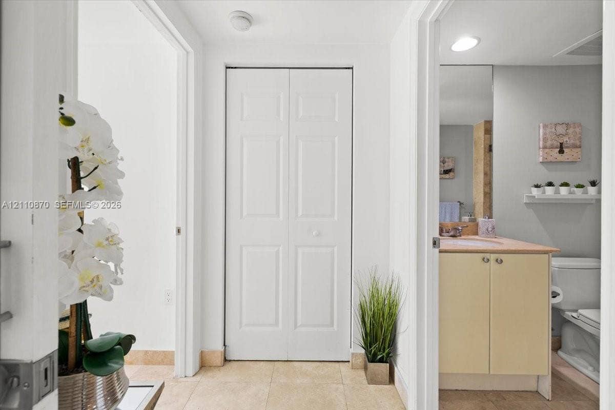 1755 E Hallandale Beach Boulevard, #MEZ5E, Hallandale Beach, FL 33009 Hallway featuring tile flooring, a white paneled closet door, and an entrance to a bathroom with a vanity, light-toned countertop, and a wall-mounted mirror