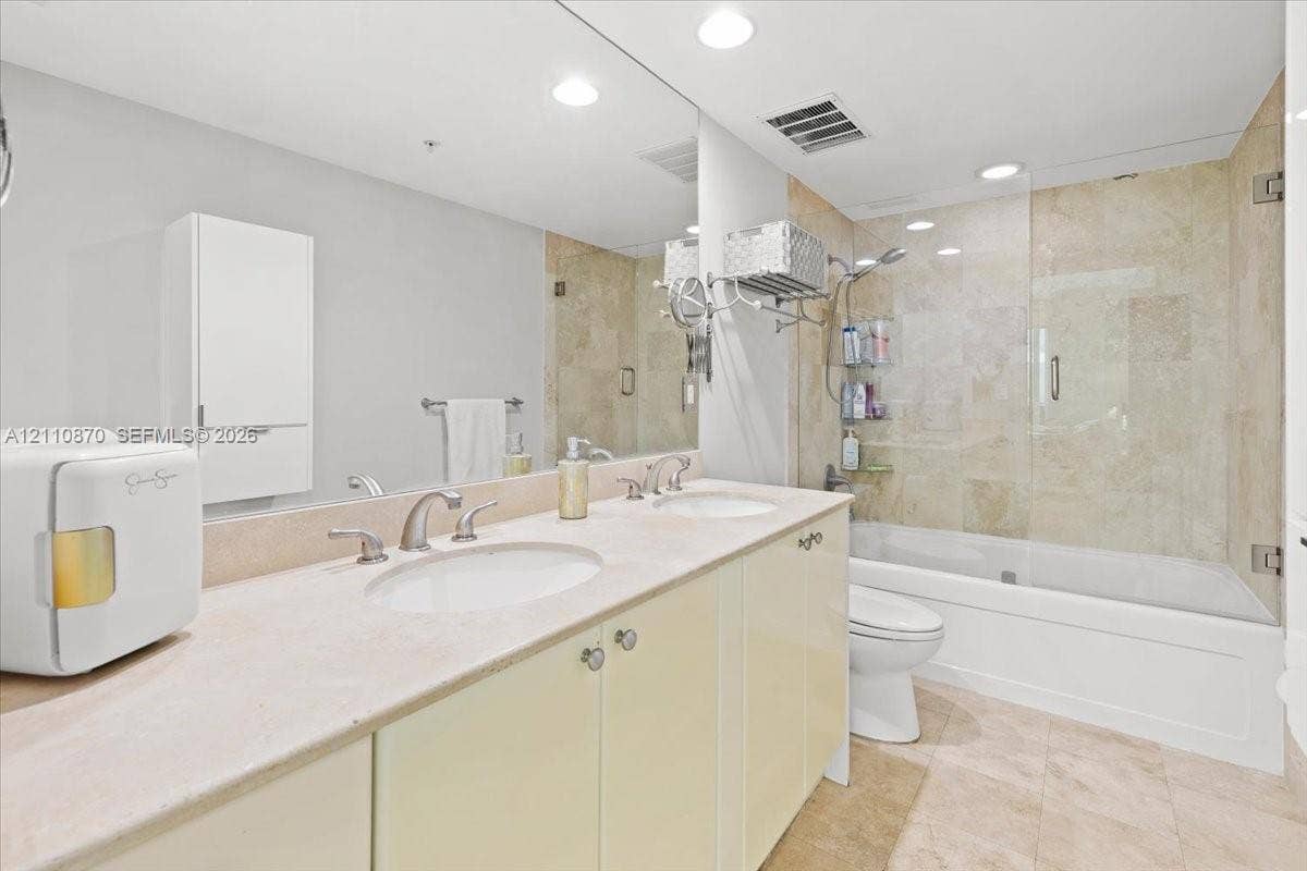 1755 E Hallandale Beach Boulevard, #MEZ5E, Hallandale Beach, FL 33009 Dual-sink vanity with stone countertop, large wall-to-wall mirror, built-in cabinetry, and a bathtub with glass enclosure and stone-tile surround