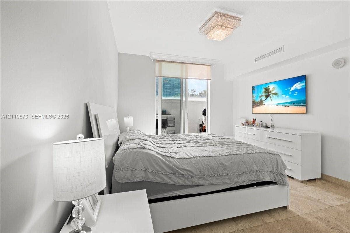 1755 E Hallandale Beach Boulevard, #MEZ5E, Hallandale Beach, FL 33009 Neutral-toned room featuring stone flooring, a multi-tiered crystal flush-mount light fixture, and floor-to-ceiling glass sliding doors with a roller shade