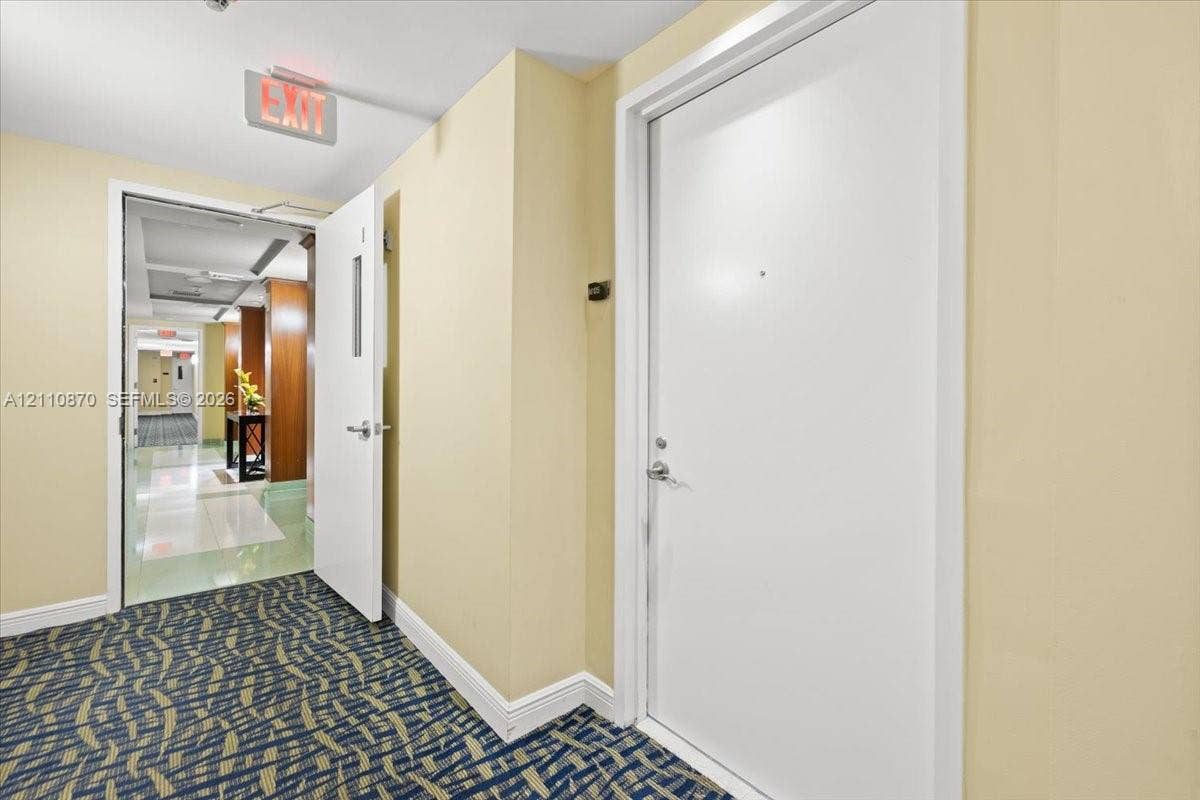 1755 E Hallandale Beach Boulevard, #MEZ5E, Hallandale Beach, FL 33009 Interior hallway featuring patterned carpeting, neutral wall paint, and white solid-core doors with metallic hardware