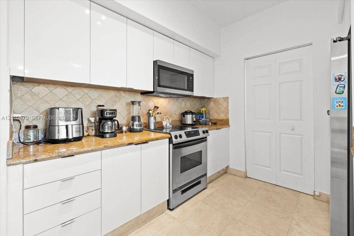 1755 E Hallandale Beach Boulevard, #MEZ5E, Hallandale Beach, FL 33009 Kitchen featuring flat-panel white cabinetry, stone-finish countertops, stainless steel appliances, tiled backsplash, and tile flooring