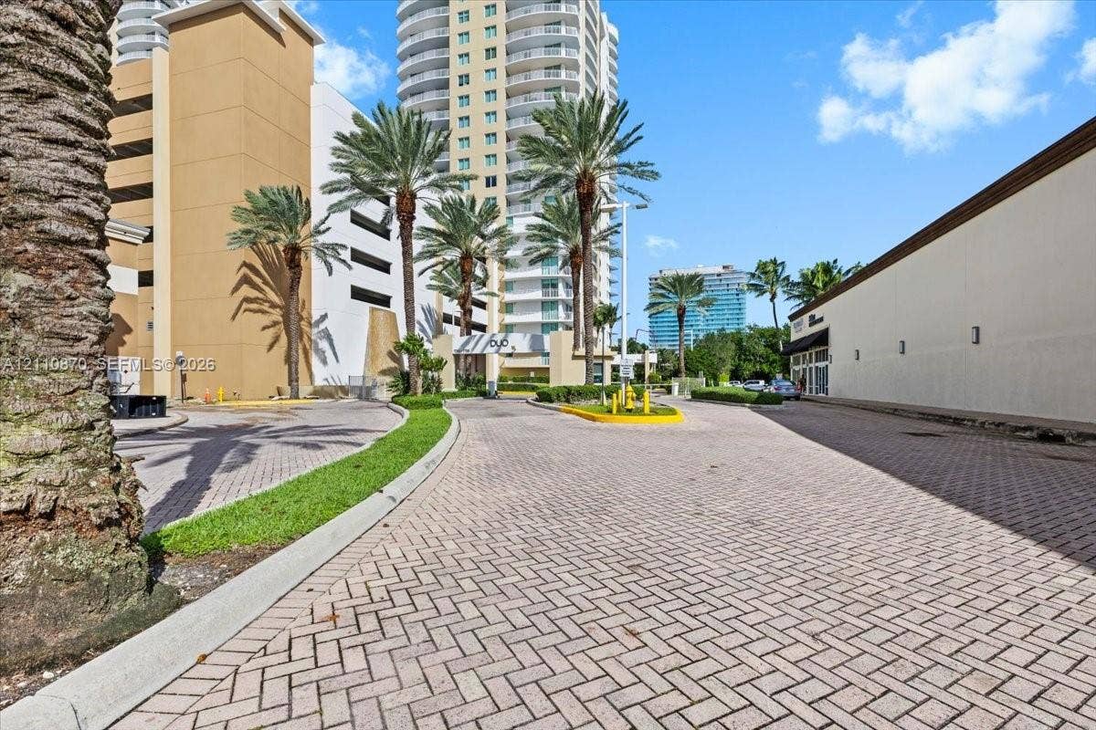 1755 E Hallandale Beach Boulevard, #MEZ5E, Hallandale Beach, FL 33009 Paver driveway featuring mature palm trees and landscaped borders