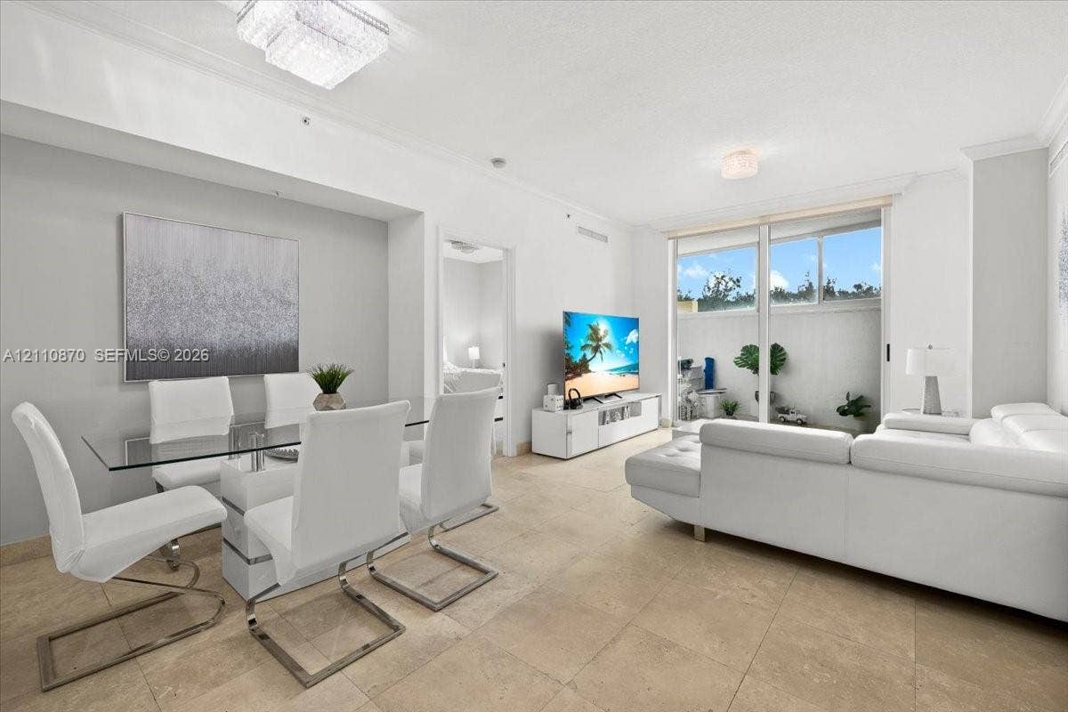 1755 E Hallandale Beach Boulevard, #MEZ5E, Hallandale Beach, FL 33009 Open-concept living space featuring large-format tile flooring, crown molding, dual flush-mount ceiling light fixtures, and expansive sliding glass doors