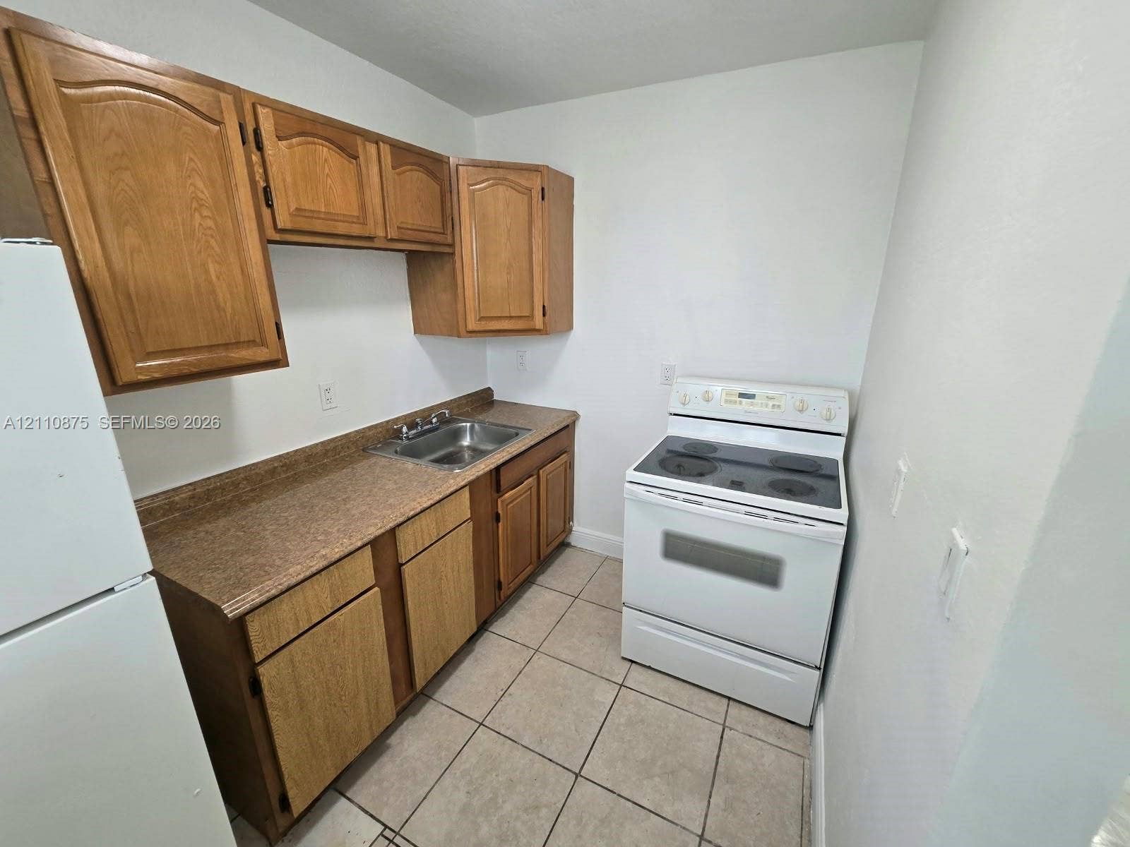 535 NW 7th Street, #10, Miami, Miami, FL 33136 Kitchen featuring wooden cabinetry, laminate countertops, a double-basin stainless steel sink, a white electric range, and tile flooring