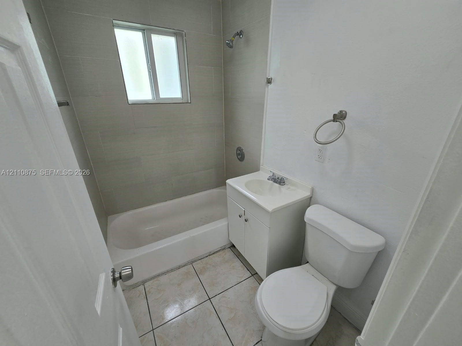 535 NW 7th Street, #10, Miami, Miami, FL 33136 Bathroom featuring light-toned tile flooring, a bathtub with a shower head, wall-mounted shower tile surround, a white vanity cabinet with an integrated basin, and a wall-mounted ring towel holder