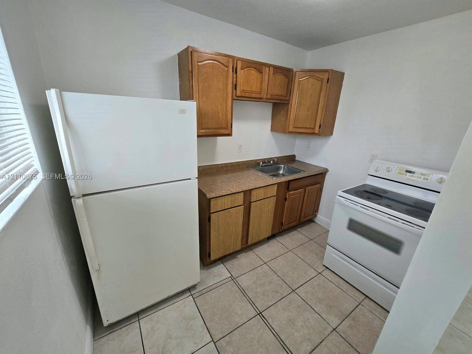 535 NW 7th Street, #10, Miami, Miami, FL 33136 Kitchen area featuring wood cabinetry, stone-finish countertops, stainless steel sink, tiled flooring, and white kitchen appliances