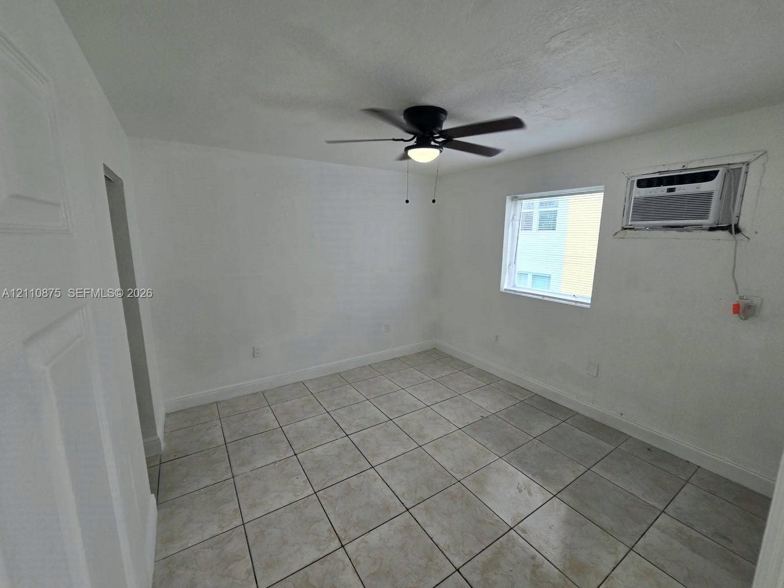 535 NW 7th Street, #10, Miami, Miami, FL 33136 Neutral-toned tile flooring, white wall finishes, black ceiling fan with integrated lighting, and a wall-mounted air conditioning unit