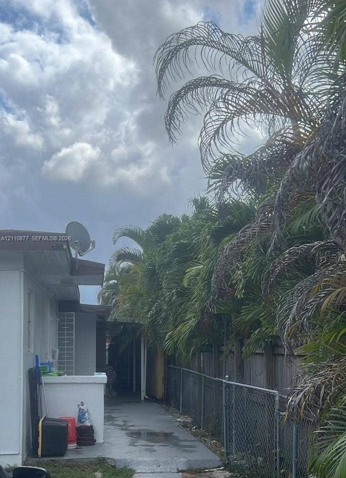 7230 NW 3rd Street, #4, Miami, Miami, FL 33126 Exterior side walkway featuring painted concrete surfacing, white stucco wall finish, and perimeter chain-link fencing bordered by mature palm trees