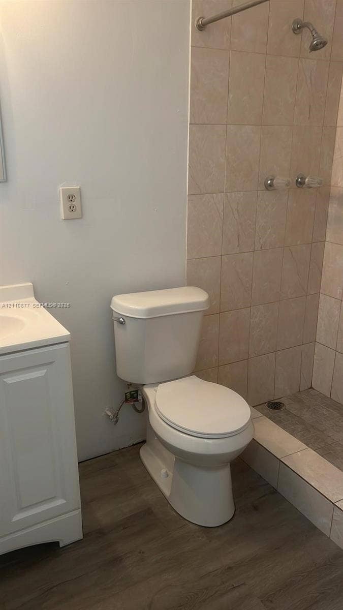 7230 NW 3rd Street, #4, Miami, Miami, FL 33126 Bathroom featuring wood-finish flooring, a white vanity cabinet, a standard-height toilet, and a shower stall with tiled walls and a metal shower head