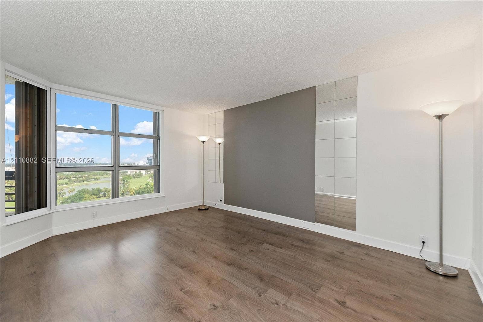 Large floor-to-ceiling bay windows, wood-finish flooring, and a decorative mirrored wall accent