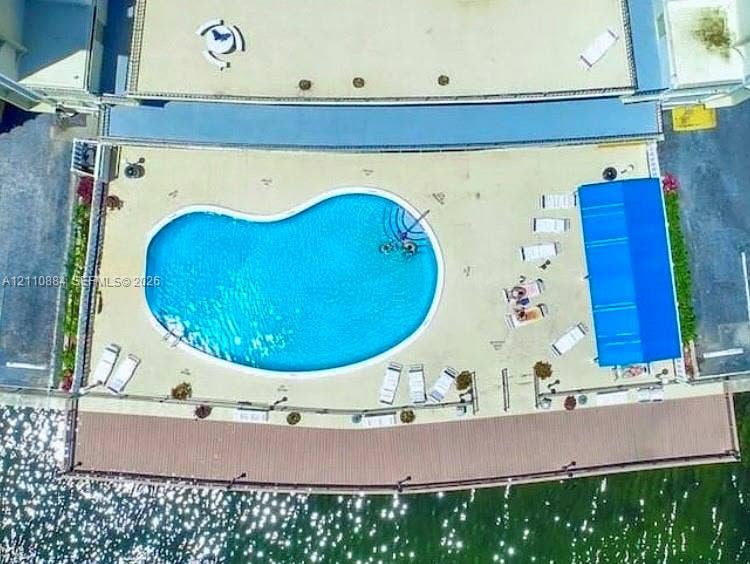 400 Diplomat Parkway, #805, Hallandale Beach, FL 33009 Kidney-shaped pool with integrated stairs, spacious paved deck, blue retractable awning, and waterfront wooden boardwalk