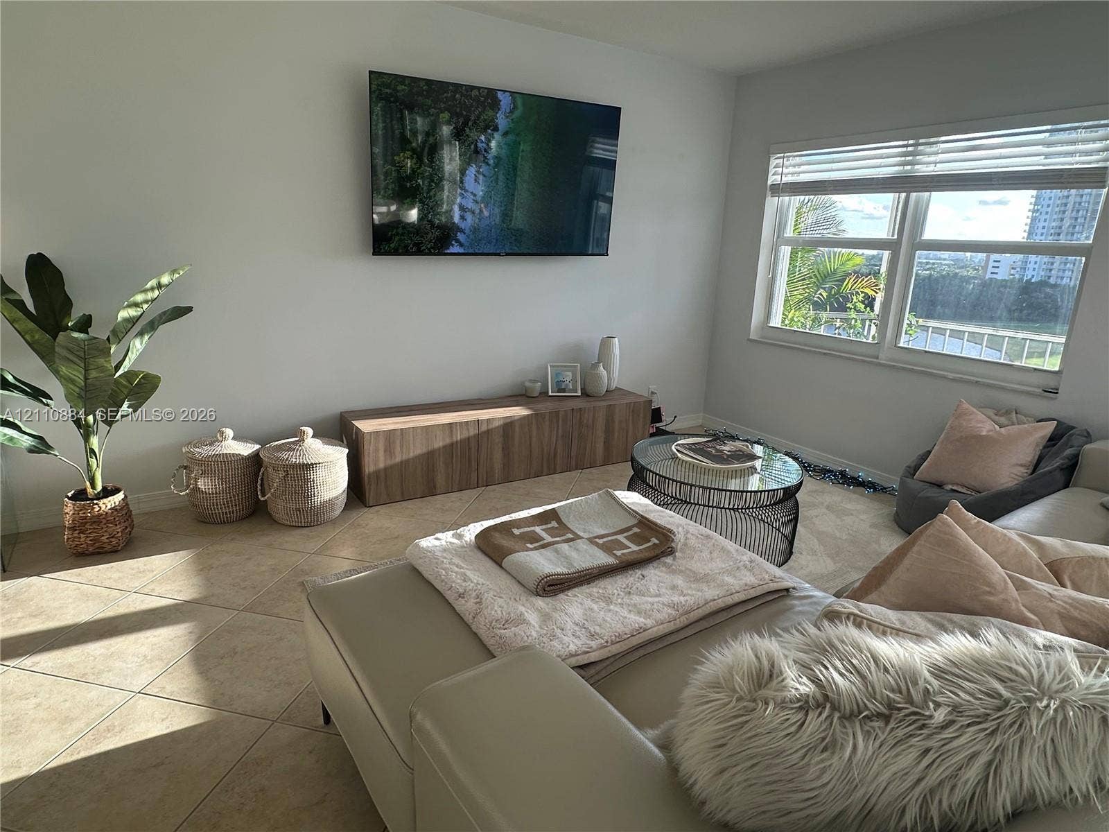 400 Diplomat Parkway, #805, Hallandale Beach, FL 33009 Neutral-tone tile flooring, wall-mounted television, built-in wood-finish cabinetry, and oversized windows with horizontal blinds