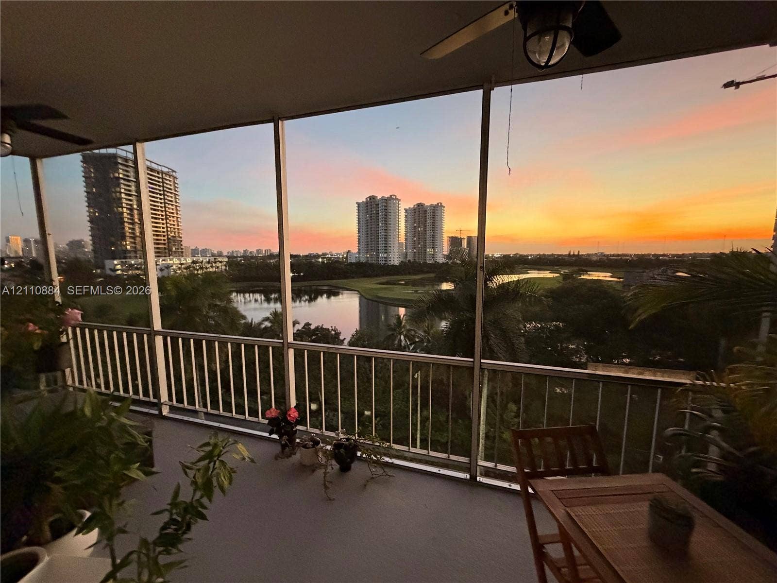 400 Diplomat Parkway, #805, Hallandale Beach, FL 33009 Screened-in balcony featuring a metal railing and ceiling-mounted fans, overlooking a lake and urban skyline