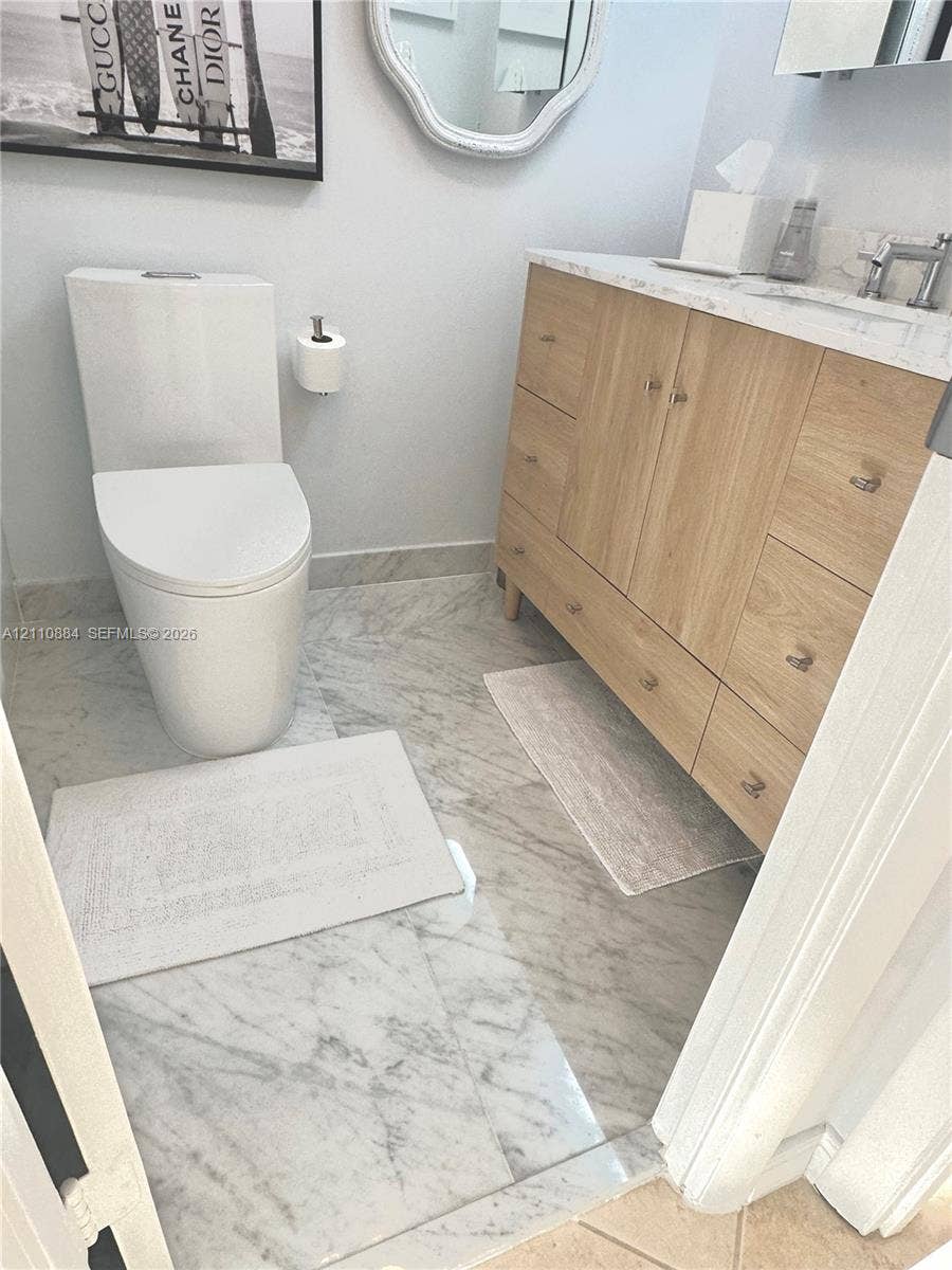 400 Diplomat Parkway, #805, Hallandale Beach, FL 33009 Light-wood cabinetry vanity featuring light-toned stone-finish countertop, integrated sink, and polished metal hardware, paired with premium Calacutta Marble stone-finish tile flooring