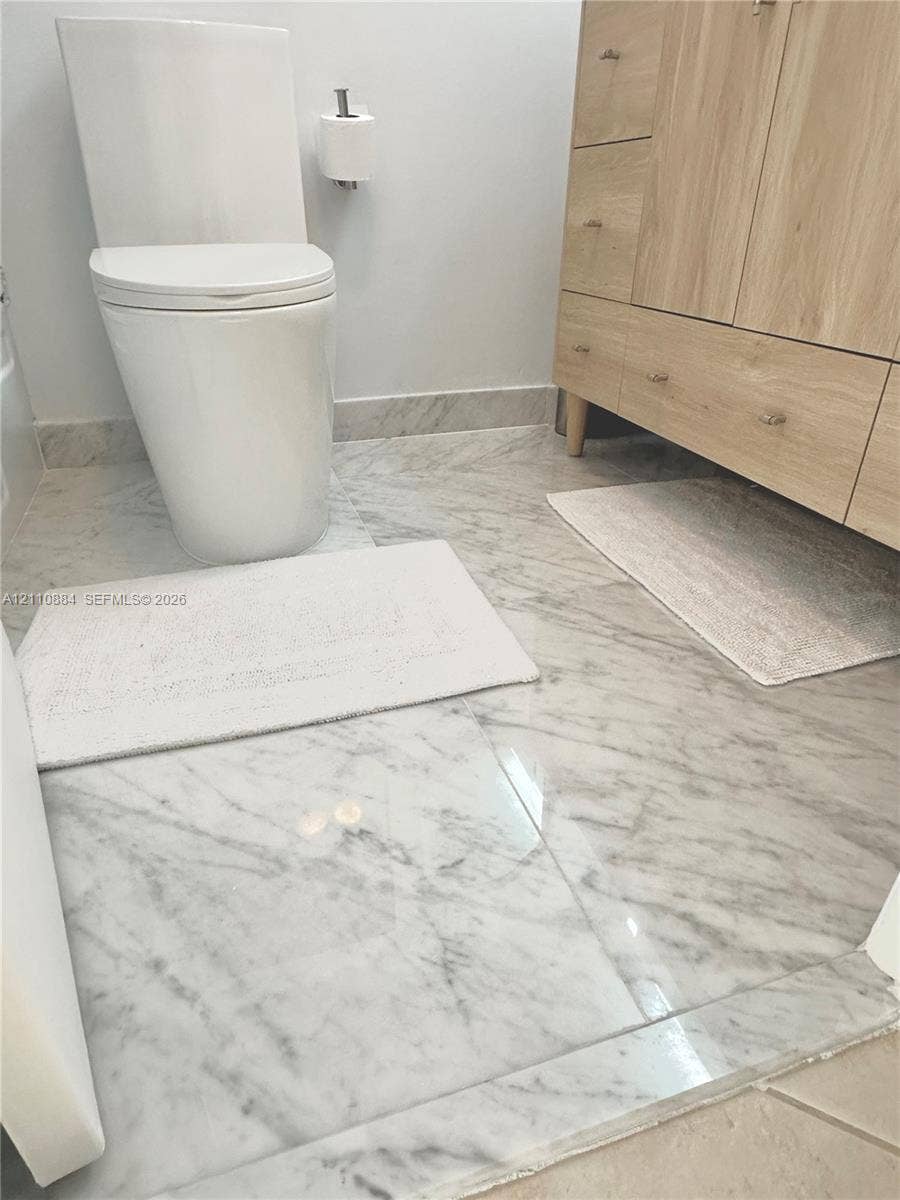 400 Diplomat Parkway, #805, Hallandale Beach, FL 33009 Bathroom featuring a wood-finish vanity with drawer cabinetry, stone-tiled flooring, and a new, ultra-modern one-piece toilet on luxe Calacutta Marble