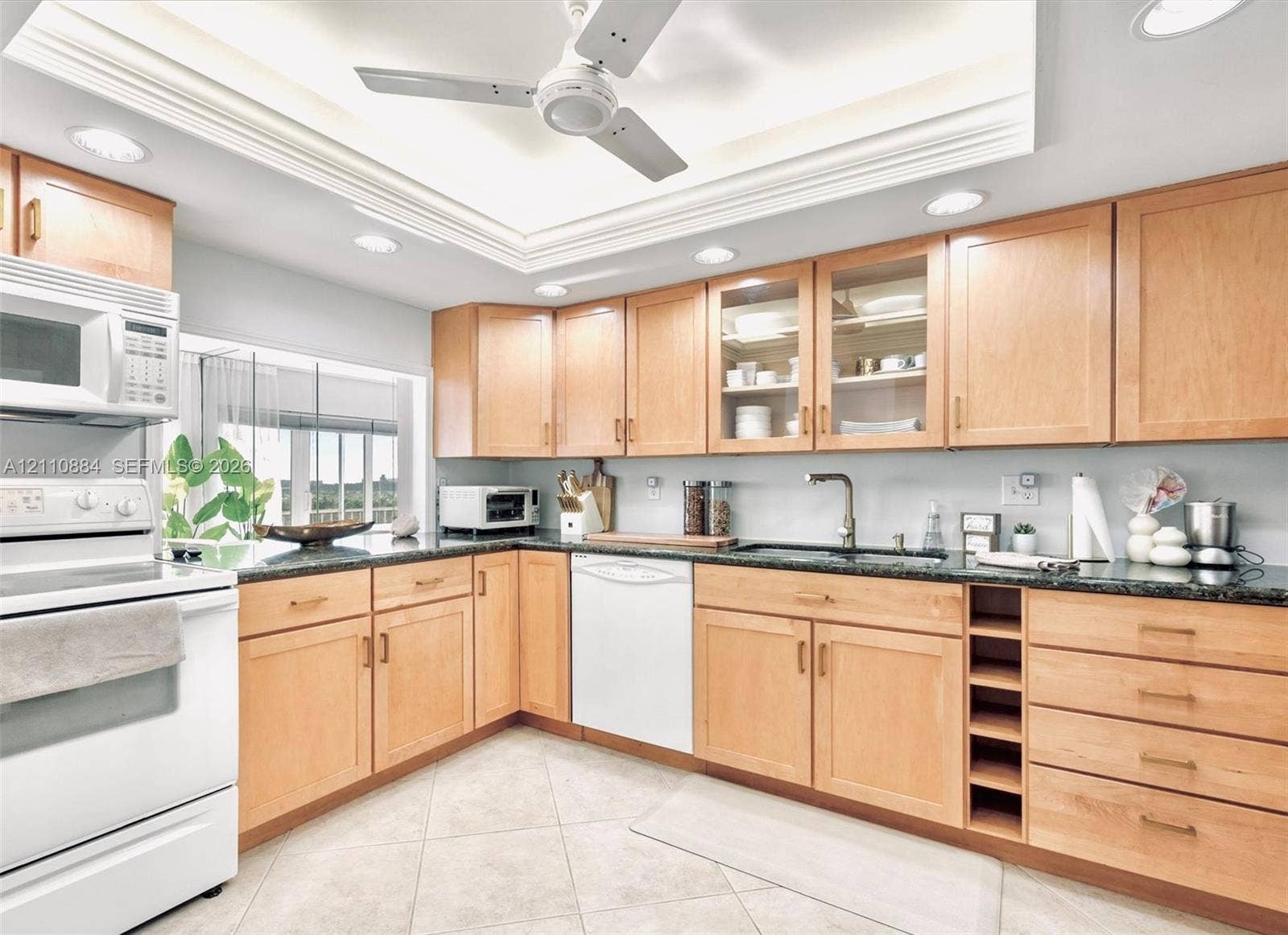 400 Diplomat Parkway, #805, Hallandale Beach, FL 33009 Kitchen featuring custom, solid maple wood cabinetry with glass-front uppers, jade stone countertops, built-in wine storage, recessed lighting, and a tray ceiling with a central ceiling fan