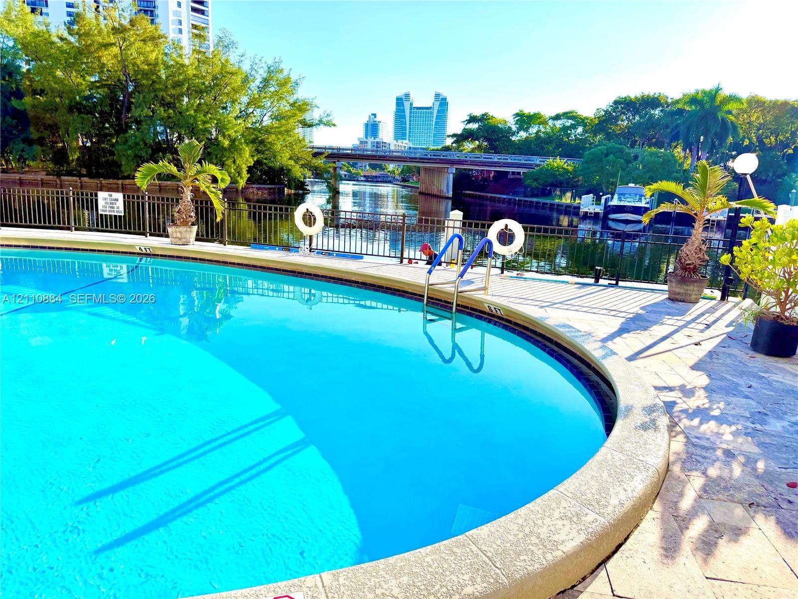 400 Diplomat Parkway, #805, Hallandale Beach, FL 33009 Curved swimming pool featuring stone-paver decking, metal perimeter fencing, and water frontage