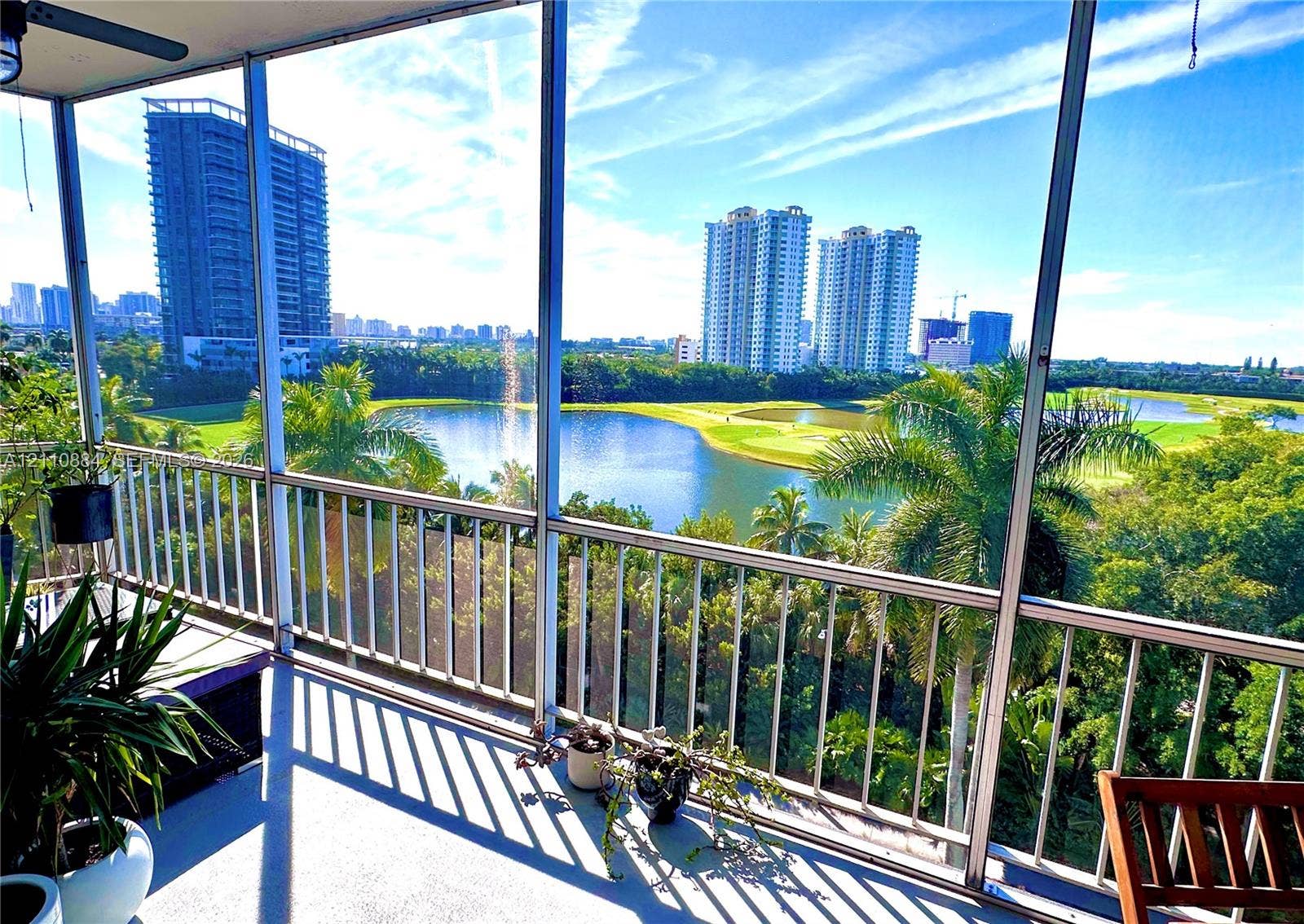 400 Diplomat Parkway, #805, Hallandale Beach, FL 33009 Screened balcony featuring metal railings, overhead ceiling fan, and concrete flooring, overlooking a lake, golf course, and tropical oasis landscape