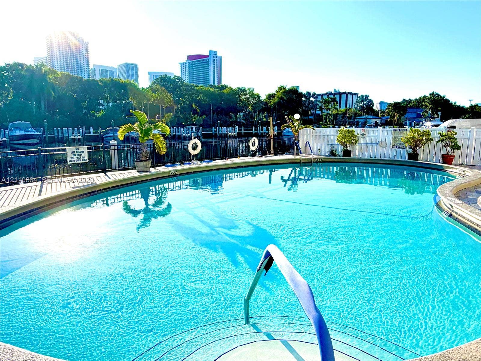 400 Diplomat Parkway, #805, Hallandale Beach, FL 33009 Curved swimming pool featuring a built-in step entry, metal perimeter fencing, and concrete decking