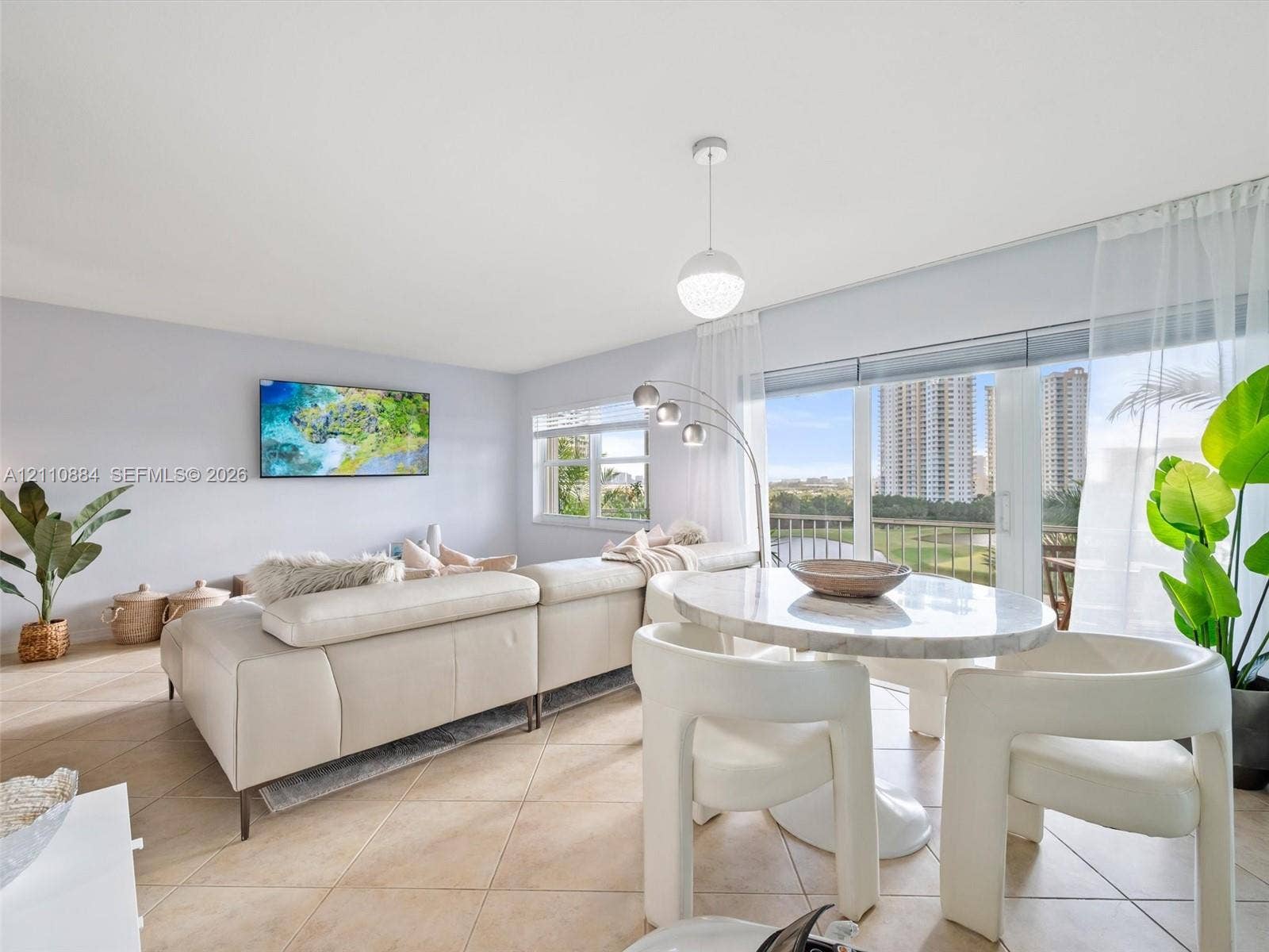 400 Diplomat Parkway, #805, Hallandale Beach, FL 33009 Open-concept living space featuring large-format diagonal tile flooring, floor-to-ceiling glass sliding doors, and a modern spherical pendant light fixture