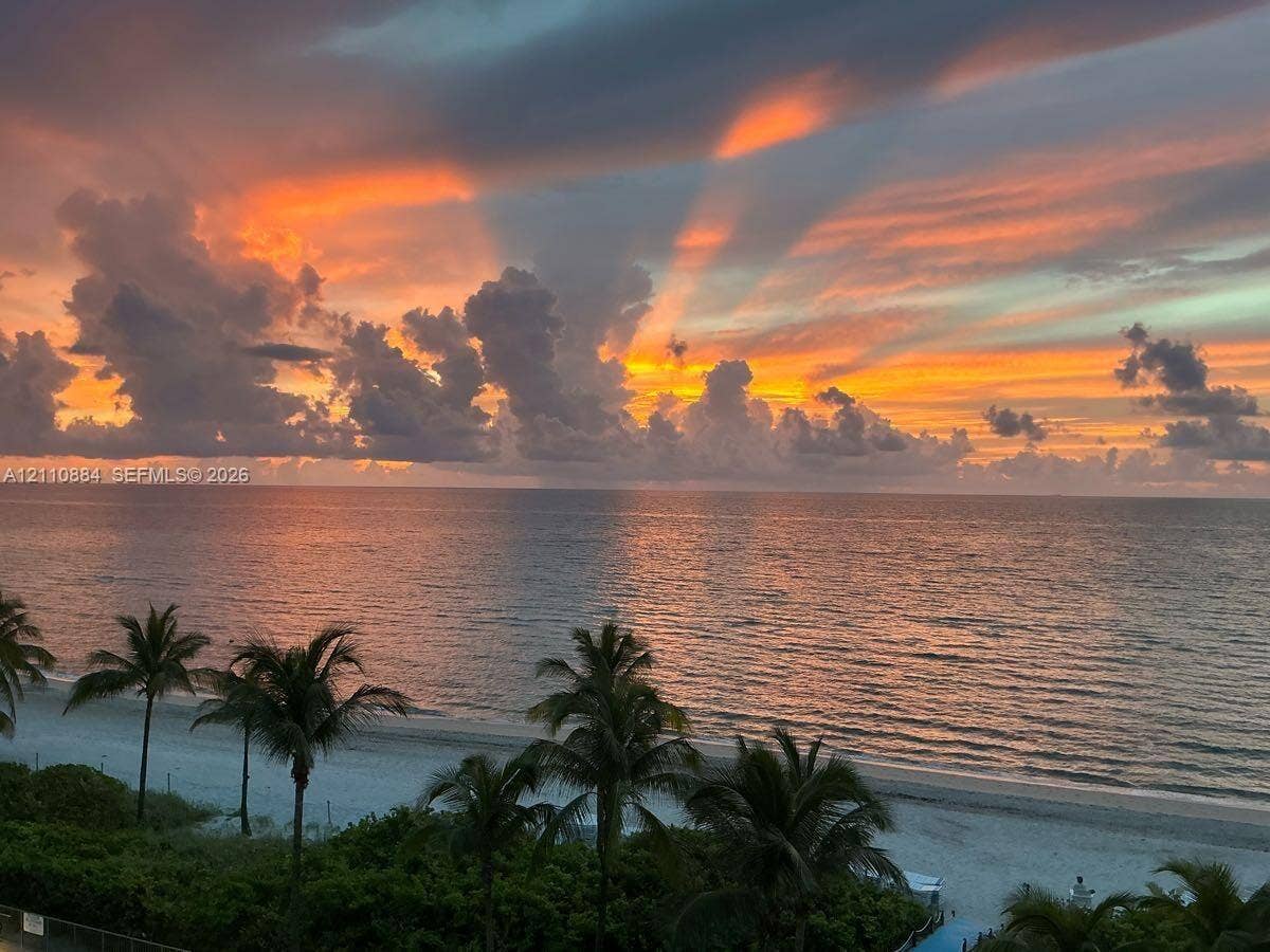 400 Diplomat Parkway, #805, Hallandale Beach, FL 33009 Direct waterfront access featuring a sandy beach, tropical palm trees, and panoramic ocean scenery at sunset