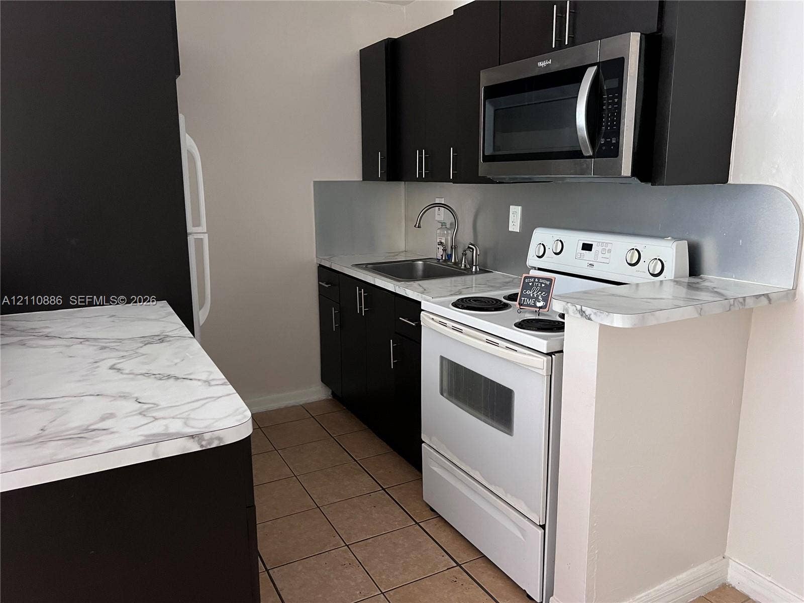 7101 Miami Lakes Drive, #Q12, Miami Lakes, Miami Lakes, FL 33014 Dark wood-finish vanity with a stone-surface countertop, oval undermount sink, white-framed wall mirror, and three-light brushed-nickel vanity fixture