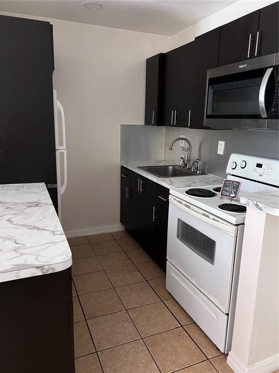 7101 Miami Lakes Drive, #Q12, Miami Lakes, Miami Lakes, FL 33014 Kitchen featuring dark cabinetry, stone-finish laminate countertops, ceramic tile flooring, and integrated stainless steel appliances