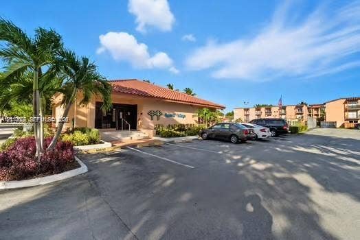 7101 Miami Lakes Drive, #Q12, Miami Lakes, Miami Lakes, FL 33014 Commercial structure featuring a terracotta tile roof, stucco exterior, paved parking area, and palm tree landscaping