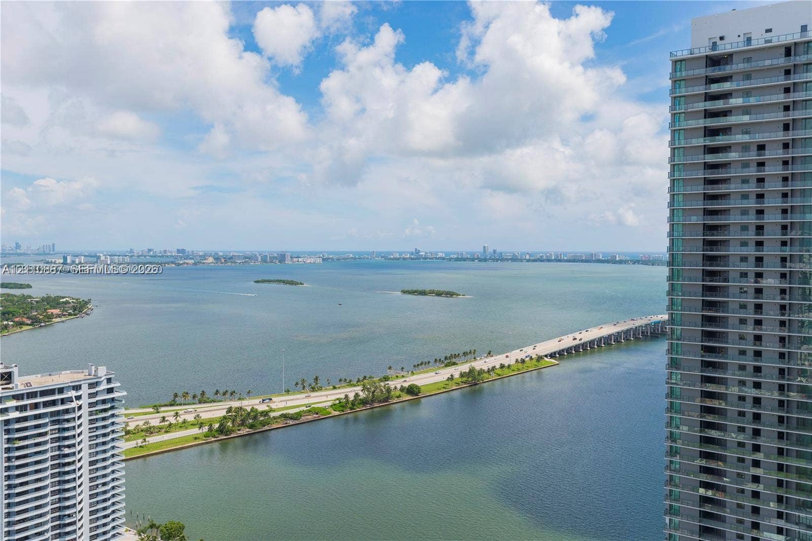 501 NE 31st Street, #4002, Miami, FL 33137 High-rise building featuring glass balcony railings and floor-to-ceiling windows, overlooking a bay, causeway, and expansive coastal horizon