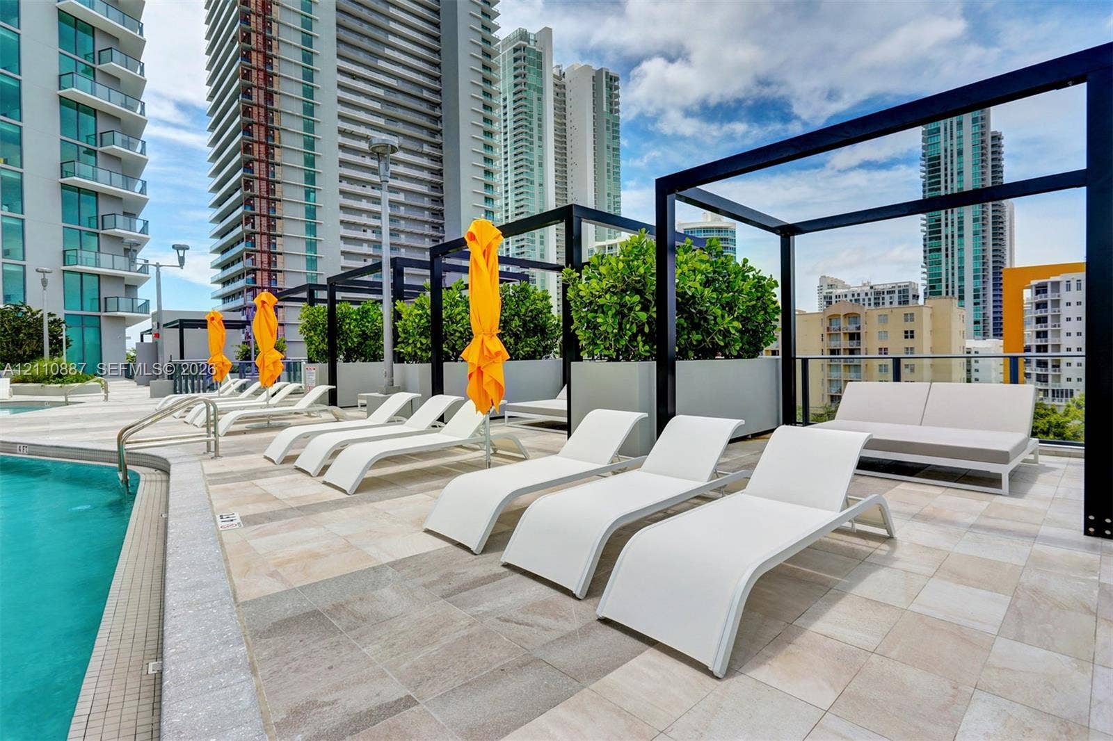 501 NE 31st Street, #4002, Miami, FL 33137 Swimming pool deck featuring stone-tiled flooring, black metal pergola structures, and integrated planter boxes with shrubbery