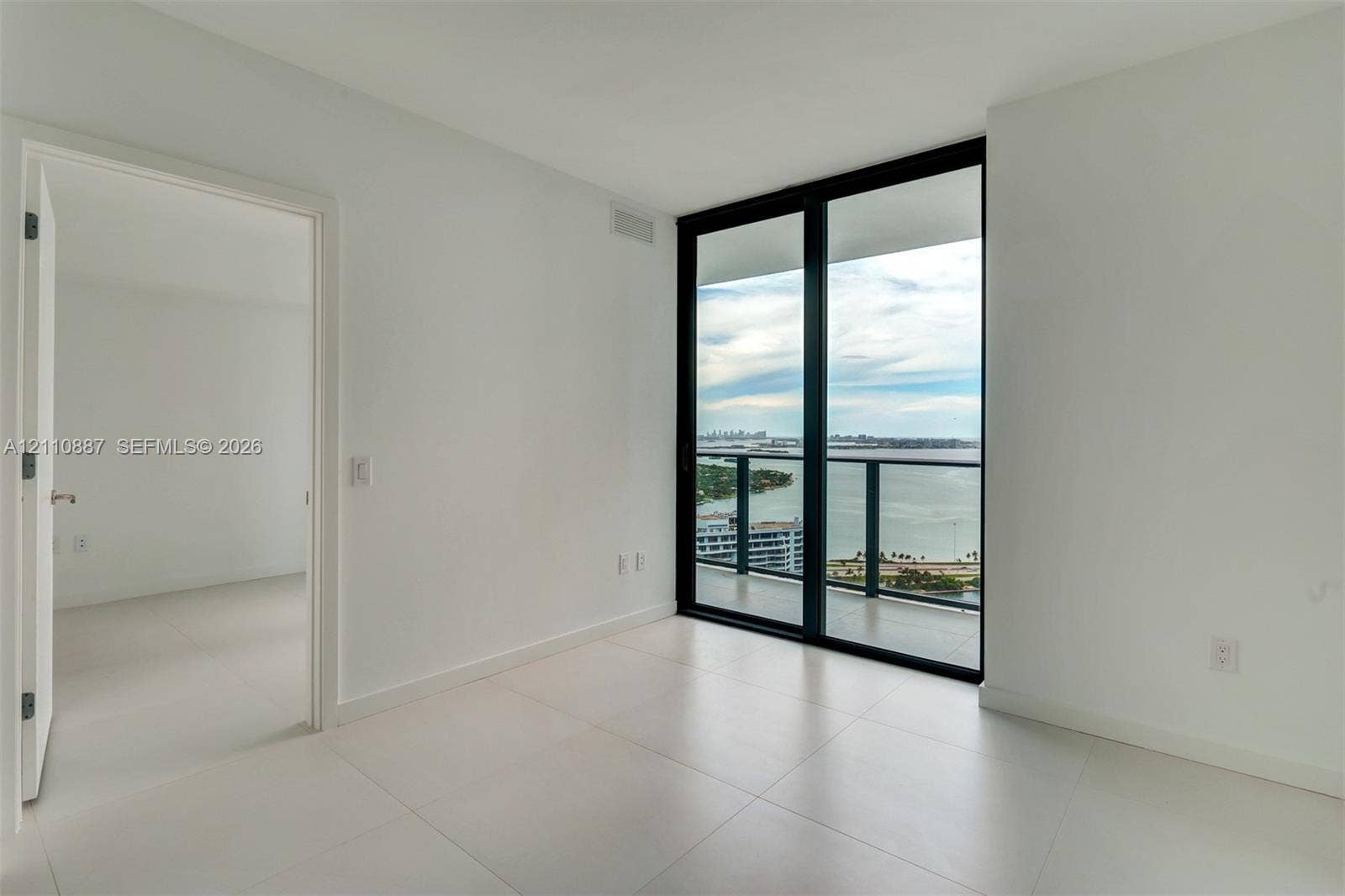 501 NE 31st Street, #4002, Miami, FL 33137 Floor-to-ceiling sliding glass doors, private balcony with metal railing, light-colored tile flooring, and neutral white wall finishes