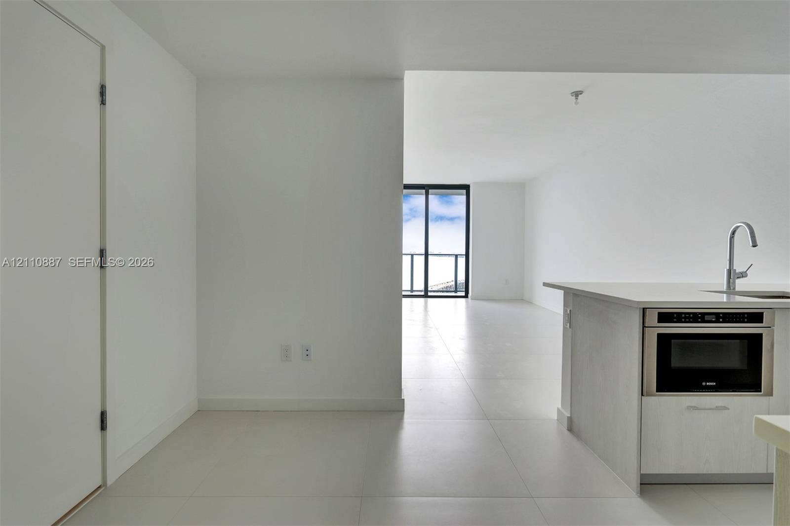 501 NE 31st Street, #4002, Miami, FL 33137 Kitchen area featuring light-finish cabinetry, quartz-style countertops, an integrated stainless steel microwave, and a stainless steel arched faucet, complemented by large-format tile flooring and floor-to-ceiling glass sliding doors