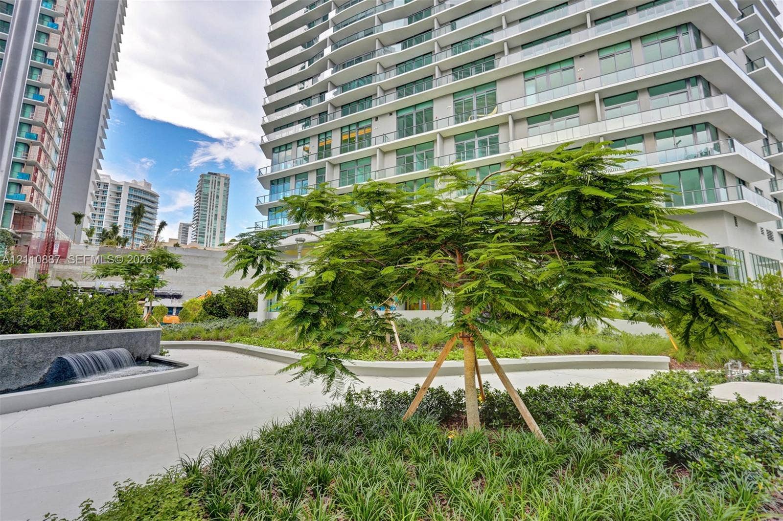 501 NE 31st Street, #4002, Miami, FL 33137 Landscaped courtyard featuring a tiered water feature, concrete walkways, mature plantings, and ornamental trees