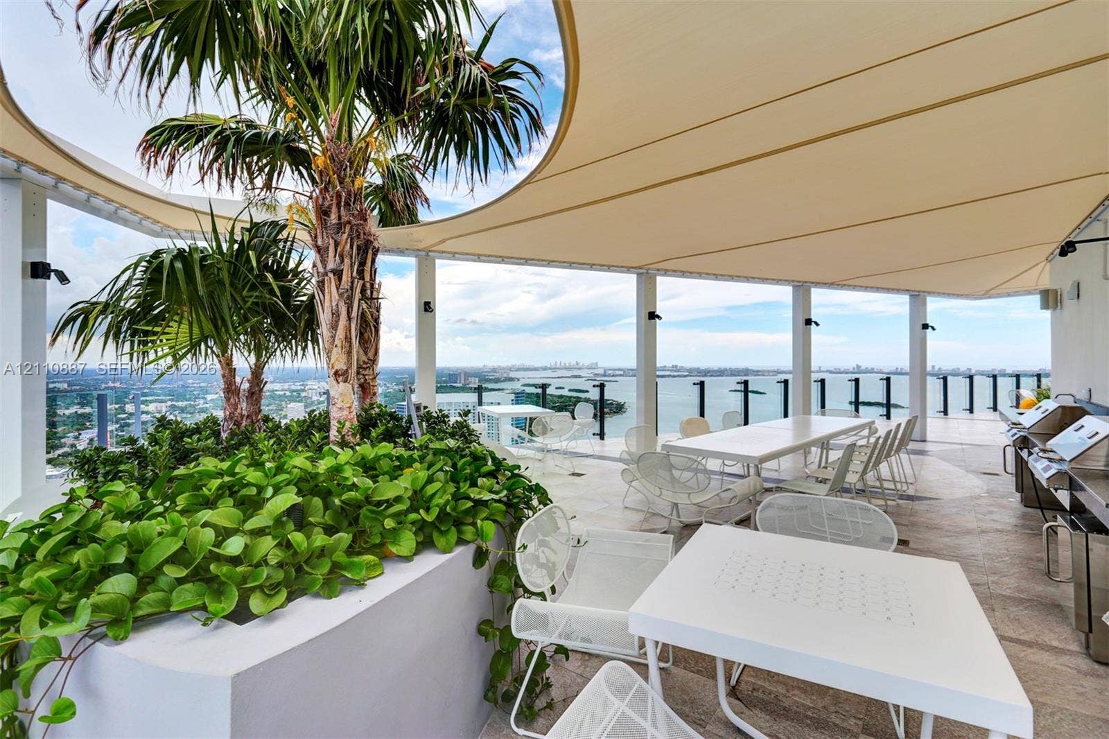 501 NE 31st Street, #4002, Miami, FL 33137 Covered rooftop terrace featuring large-format stone tile flooring, a custom-fitted tension shade structure, built-in concrete planter beds, and a stainless steel outdoor kitchen station