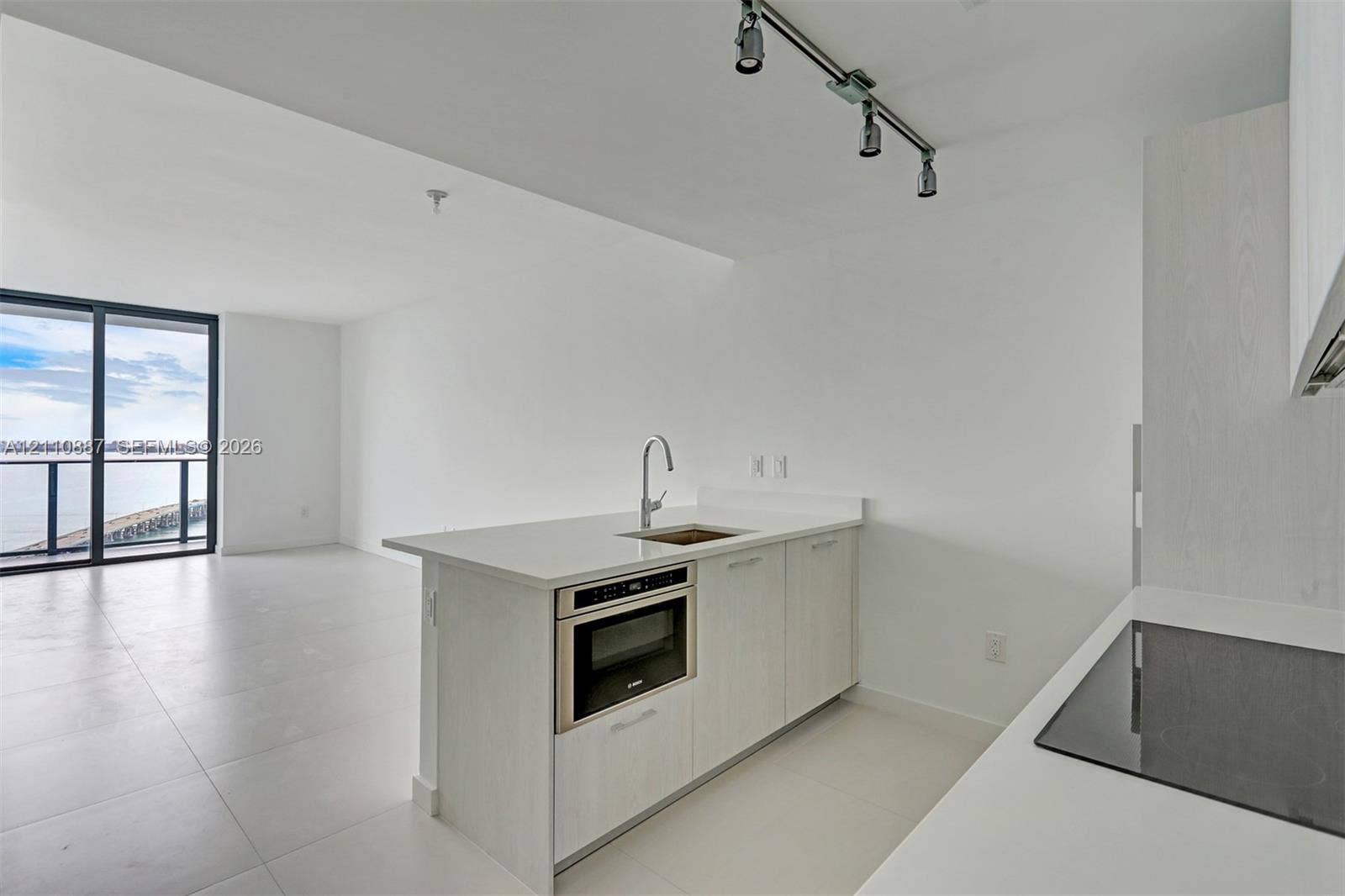 501 NE 31st Street, #4002, Miami, FL 33137 Kitchen featuring light-toned cabinetry, solid-surface countertops, built-in microwave, flat-panel cooktop, and track lighting
