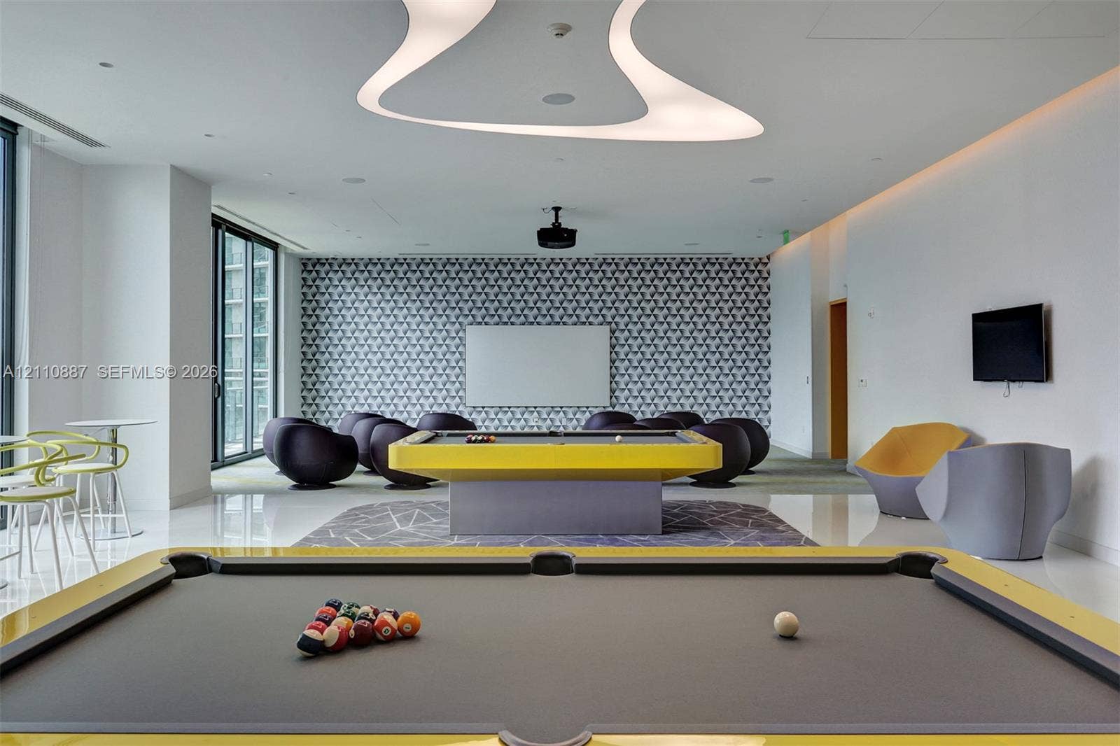 501 NE 31st Street, #4002, Miami, FL 33137 Recreation room featuring an abstract recessed ceiling light fixture, patterned accent wall, sleek flooring, and floor-to-ceiling glass paneling