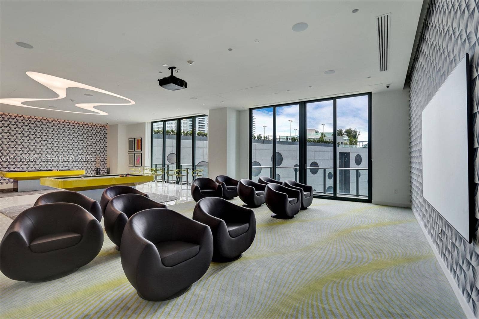 501 NE 31st Street, #4002, Miami, FL 33137 Multi-purpose room featuring textured wall panels, floor-to-ceiling glass sliding doors, custom overhead sculptural lighting, integrated ceiling speakers, and a ceiling-mounted projector