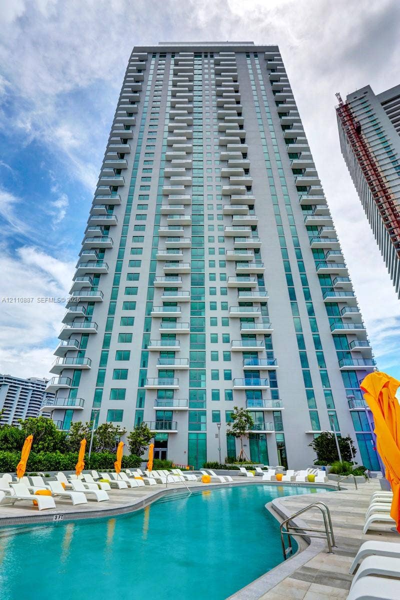 501 NE 31st Street, #4002, Miami, FL 33137 High-rise residential tower featuring tiered glass-railed balconies, exterior masonry facade, and an outdoor swimming pool with stone-tiled decking