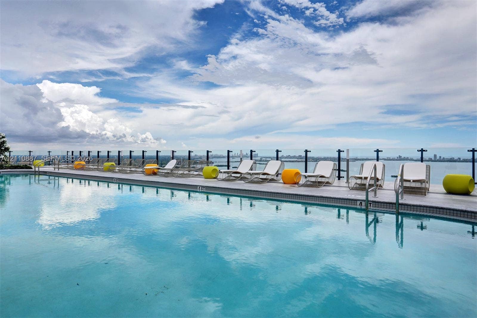 501 NE 31st Street, #4002, Miami, FL 33137 Infinity-edge pool featuring a glass-panel railing, tiled perimeter, and water-level entry steps