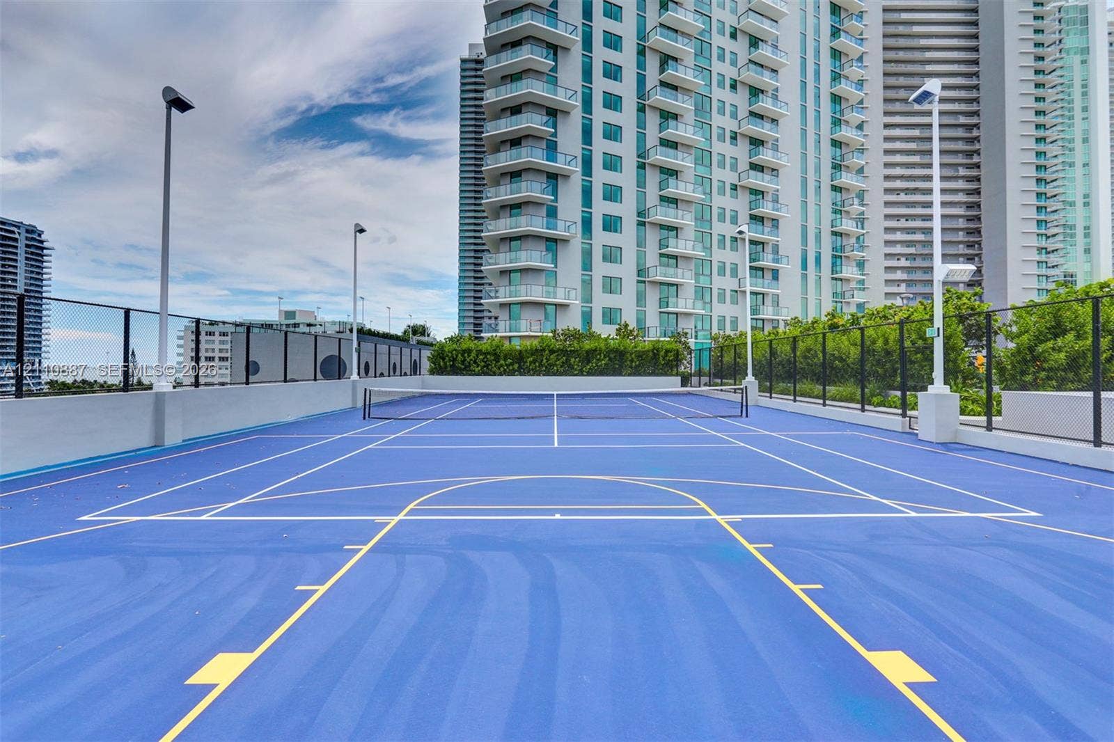 501 NE 31st Street, #4002, Miami, FL 33137 Multi-use sports court with a blue surface, painted court markings, permanent net system, high-pole lighting, and perimeter fencing