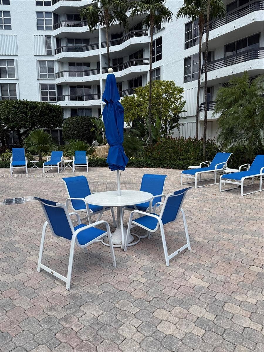 3600 Mystic Pointe Drive, #1611, Aventura, FL 33180 Paver patio featuring integrated landscaping, palm trees, and multi-story building exterior