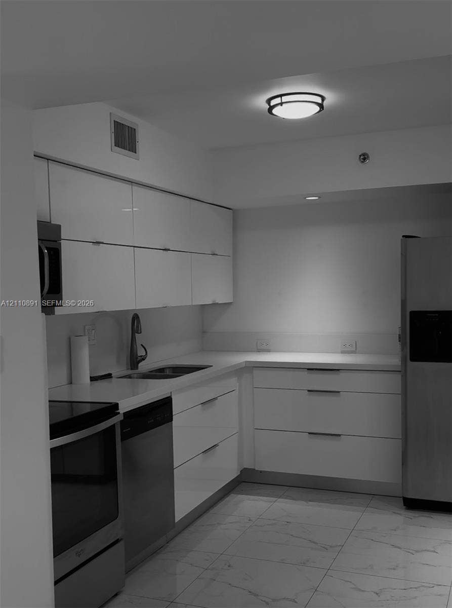 3600 Mystic Pointe Drive, #1611, Aventura, FL 33180 Kitchen featuring glossy flat-panel cabinetry, light-toned stone-finish countertops, stainless steel appliances, stone-finish tile flooring, and flush-mount ceiling lighting