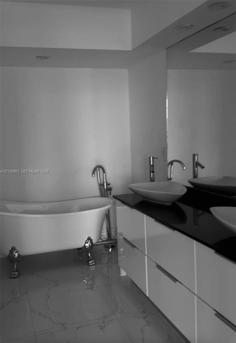 3600 Mystic Pointe Drive, #1611, Aventura, FL 33180 Freestanding clawfoot tub with floor-mounted faucet, dual vessel sinks, dark stone countertop, high-gloss white vanity cabinetry, and large-format tile flooring