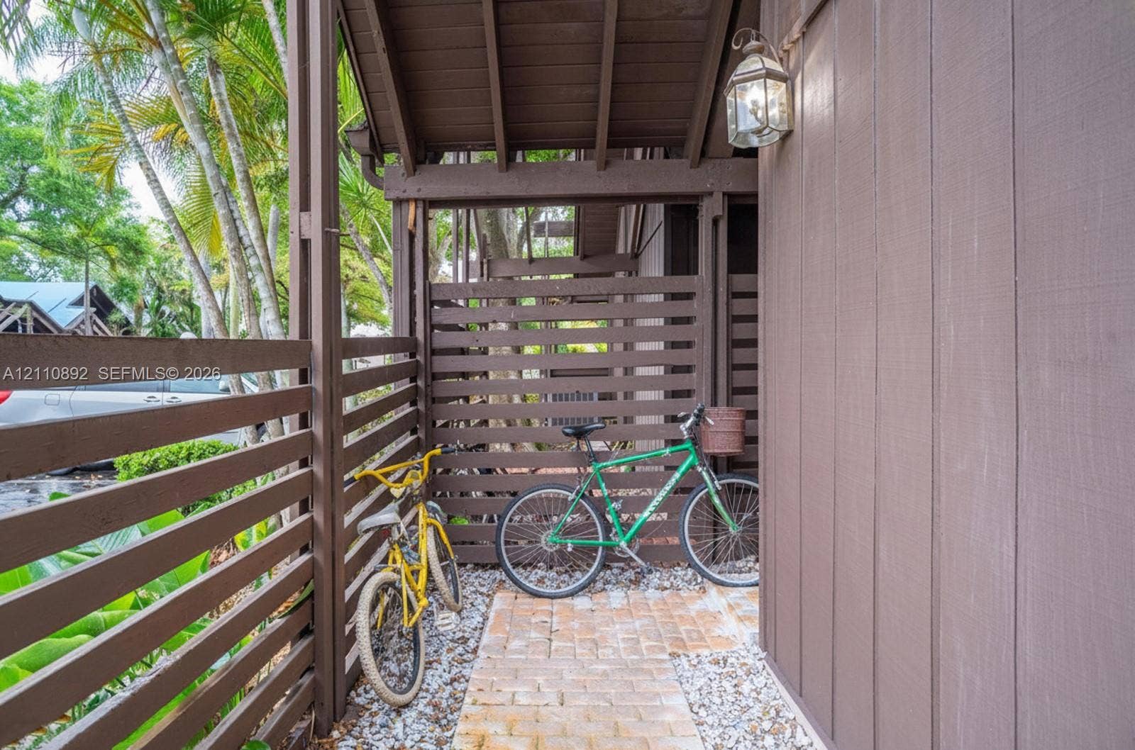 497 N University Drive, #2-7, Plantation, FL 33324 Covered entryway featuring vertical wood siding, horizontal slat privacy fencing, brick paver ground surface, and an exterior wall-mounted carriage-style light fixture
