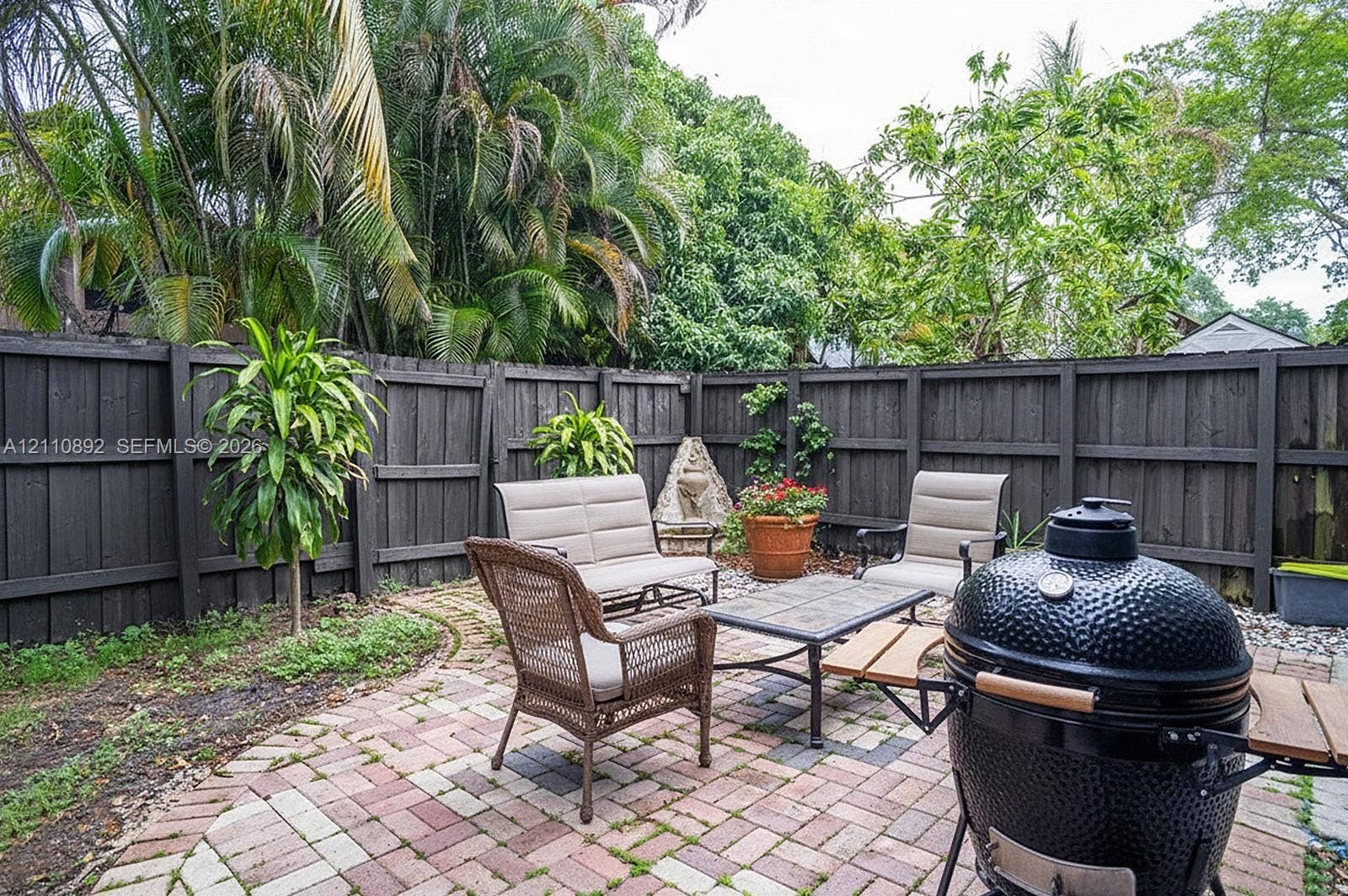 497 N University Drive, #2-7, Plantation, FL 33324 Private courtyard featuring a patterned brick paver patio, dark wood-finish perimeter fencing, and established tropical landscaping